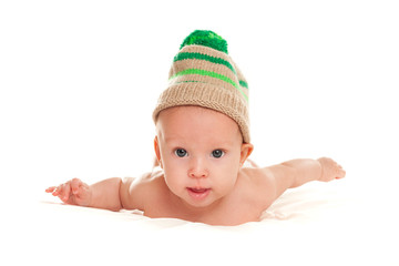 baby newborn lying on her stomach on the bed in a funny knitted hat isolated on white background, the concept of choosing baby clothes, washing and care