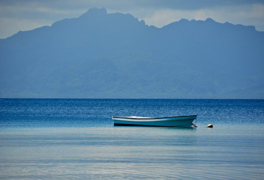 Solitary boat sits quietly in calm blue water with tropical mountains in the background 
