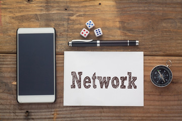 Network Word written on white on wooden desk with dice,compass,smart phone and pen.Top view conceptual