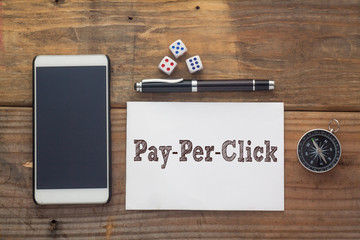 Pay Per Click Words written on white on wooden desk with dice,compass,smart phone and pen.Top view conceptual