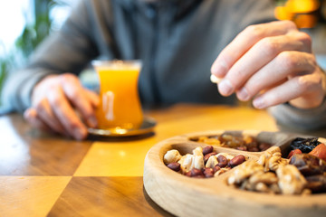 Obraz na płótnie Canvas A man eats nuts and drinks tea in cafe. Wooden plate with nuts and dried fruits. Turkish sweets.