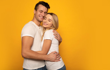Warm feelings. Close-up photo of a cute couple, hugging tightly and smiling while posing on a yellow background.