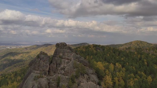 Aerial view of a group of tourists on top of a high cliff in the autumn forest. Free solo climbing in Siberian nature reserve Stolby. Stolbizm.