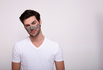A young male model with a clay mask on his face stands on a white background.