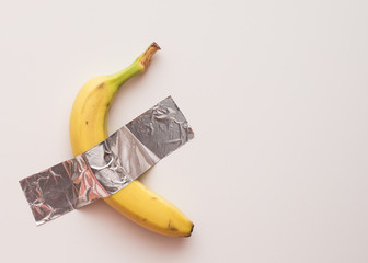 Yellow ripe banana on the wall glued with tape. Conceptual photo.