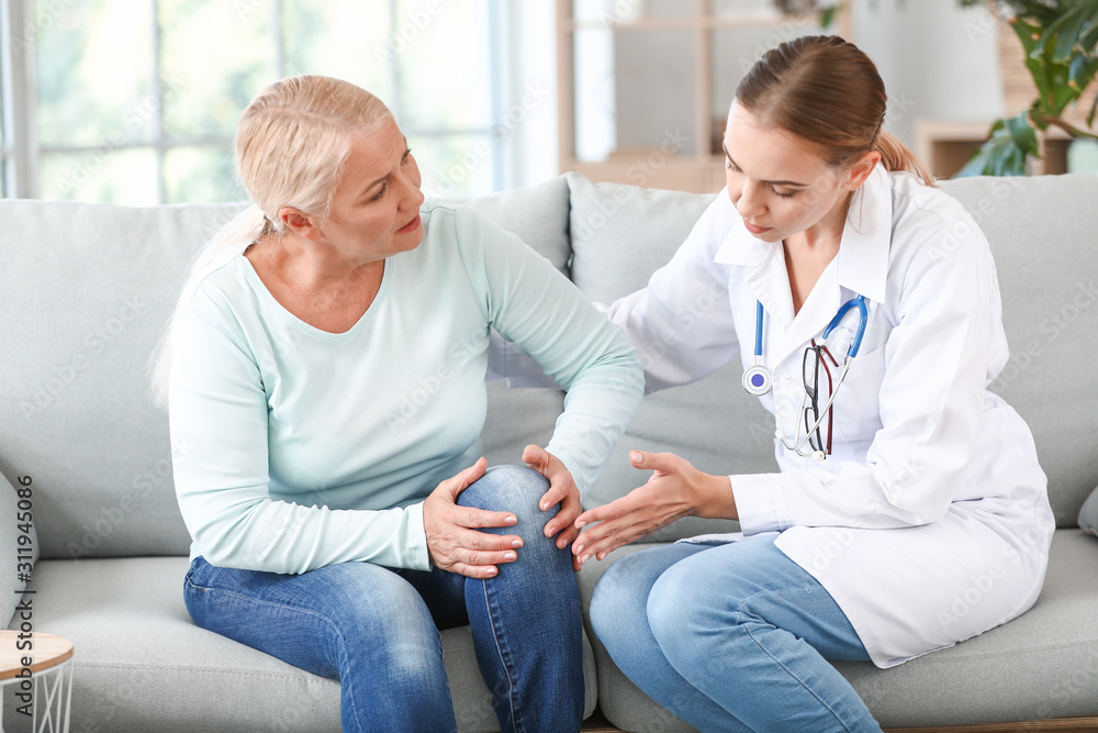 Wall mural doctor examining mature woman with joint pain at home