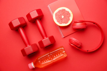 Fototapeta na wymiar Dumbbells with notebook, headphones grapefruit and bottle of water on color background