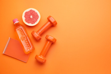Dumbbells with notebook, grapefruit and bottle of water on color background