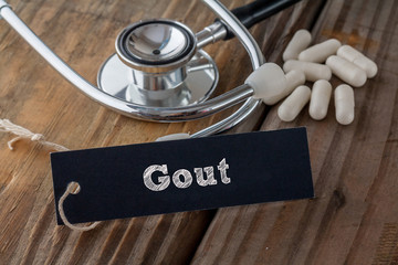Gout written on label tag with pills and Stethoscope on wood background
