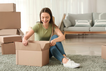 Happy young woman unpacking moving box in new house