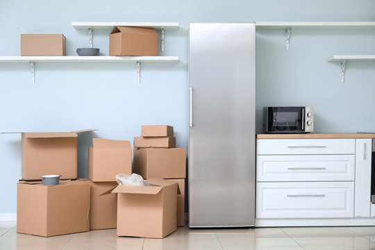 Cardboard boxes with belongings and fridge in kitchen of new flat on moving day