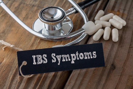IBS Symptoms written on label tag with pills and Stethoscope on wood background