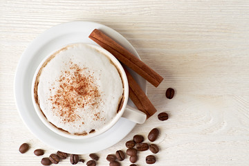 Cup of cappuccino with coffee beans and cinnamon sticks on white