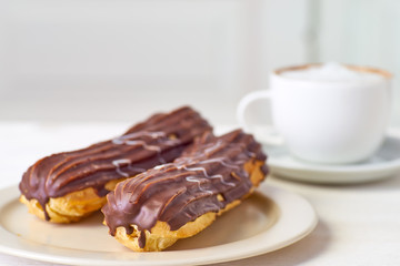 Dish with two eclairs and cup of coffee on white wooden table