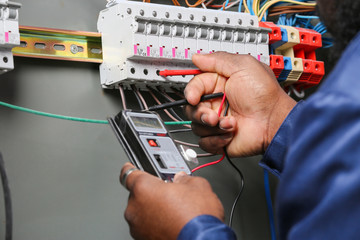 African-American electrician performing wiring in distribution board, closeup