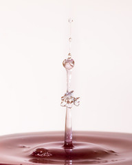 A macro photo of two drops of water colliding in a pool of red colored water captured using a flash...