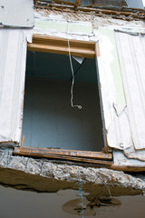 A window without glass in a ruined house and a hanging wire.