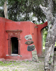 A red adobe dwelling built with rocks in a tree.