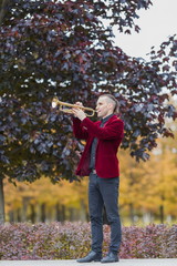 young trumpeter in red velvet jacket plays autumn melody on his musical instrument trumpet or horn...