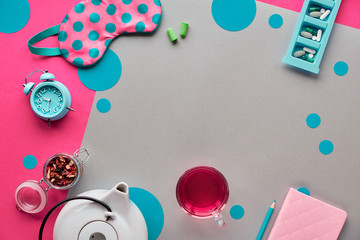 Obraz premium Sleeping mask, alarm clock, earphones and earplugs. Calming remedies - pills, capsules and bed time tea. Sleep diary or log notebook with pencil. Flat lay, two tone pink and craft paper flat lay..