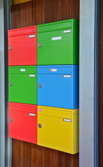 Two columns of six colorful mail boxes, hanging on a dark wooden wall. Postbox or Mail Letterbox for Condominium Exterior, Apartment Equipment Tool Object.