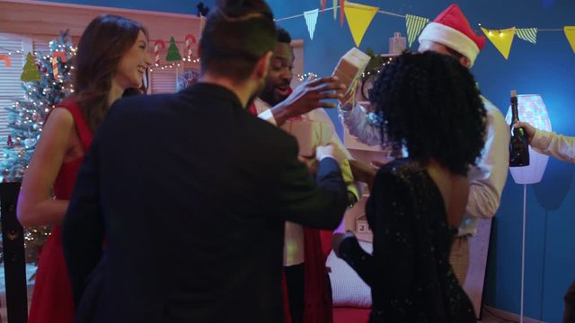 Happy handsome african man is having a holiday suprise from friends receiving Christmas gifts and warm hugs embracing in circle celebrating modern New Year party.