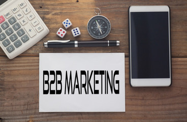 B2B Marketing written on paper,Wooden background desk with calculator,dice,compass,smart phone and pen.Top view conceptual.