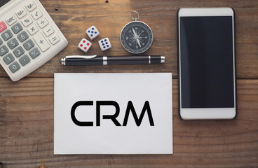 CRM Business Customer  written on paper,Wooden background desk with calculator,dice,compass,smart phone and pen.Top view conceptual.