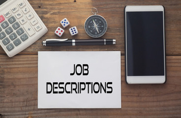 Job Descriptions written on paper,Wooden background desk with calculator,dice,compass,smart phone and pen.Top view conceptual.