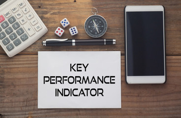 Key Performance Indicator written on paper,Wooden background desk with calculator,dice,compass,smart phone and pen.Top view conceptual.