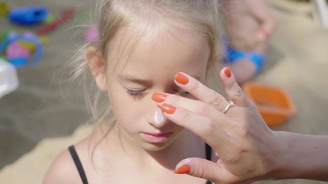 Mother applying sunscreen protection cream on cute daughter during summer sea vacation. Children healthcare at travel time.