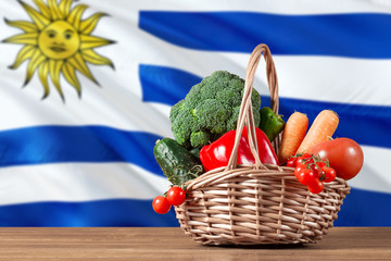 Uruguay organic food concept. National flag background with basket full of vegetables on wooden table. Copy space for text.
