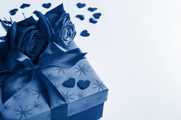 gift box with ribbon, roses and little hearts colored in trendy color of year 2020 Classic Blue, concept of Valentine's day, anniversary, mother's day or birthday greeting, copy space.