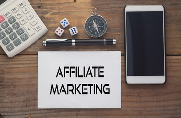 Affiliate Marketing written on paper,Wooden background desk with calculator,dice,compass,smart phone and pen.Top view conceptual.