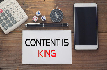 Content Is King written on paper,Wooden background desk with calculator,dice,compass,smart phone and pen.Top view conceptual.