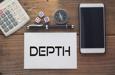 Depth written on paper,Wooden background desk with calculator,dice,compass,smart phone and pen.Top view conceptual.