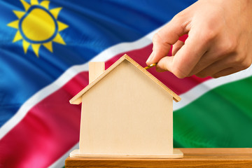 Namibia home savings concept. Close-up of hand inserting coin in the wooden house on wooden table...