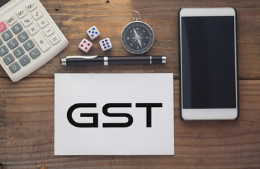 GST written on paper,Wooden background desk with calculator,dice,compass,smart phone and pen.Top view conceptual.