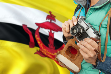 Brunei photographer concept. Close-up adult woman holding retro camera on national flag background. Adventure and traveler theme.