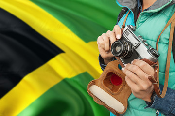 Jamaica photographer concept. Close-up adult woman holding retro camera on national flag background. Adventure and traveler theme.