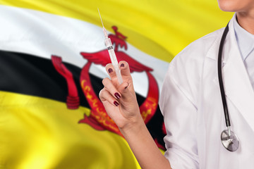 Brunei surgery injection concept. Woman doctor or nurse look at syringe needle on national flag background. Health care theme, copy space for text.