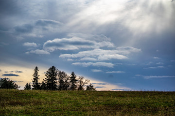 Dramatic clouds over empty midwestern field with sunburst and evergreens