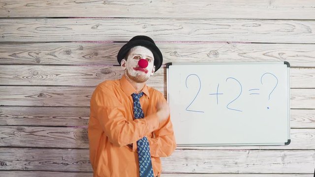 Portrait of cute male clown near the school or student blackboard. Stupid teacher explaining to students the task