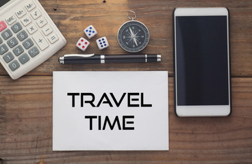 Travel Time written on paper,Wooden background desk with calculator,dice,compass,smart phone and pen.Top view conceptual.