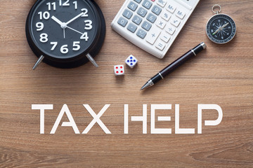 Tax Help written conceptual,alarm clock,dice,pen,calculator and compass on wood background