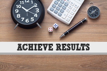 ACHIEVE RESULTS written conceptual,alarm clock,dice,pen,calculator and compass on wood background