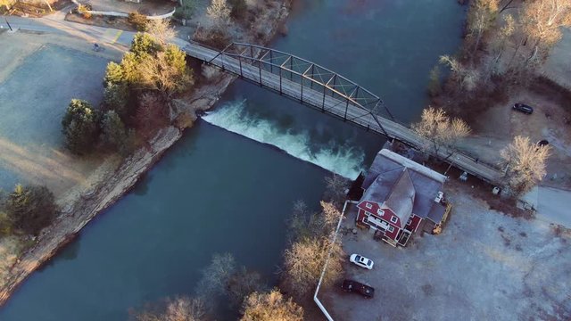 aerial view of working grist mill with paddle wheel turned by river spanned by an old iron bridge