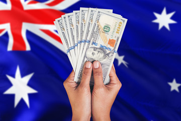 Australia financial concept. Female hand holding dollar banknotes on national flag background....