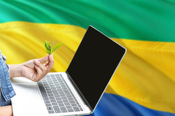 Gabon modern agriculture concept. Farmers holding laptop, check tea on national flag background....