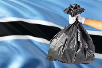 Botswana environmental protection concept. The male hand holding a garbage bag on national flag background. Ecological and recycling theme with copy space.